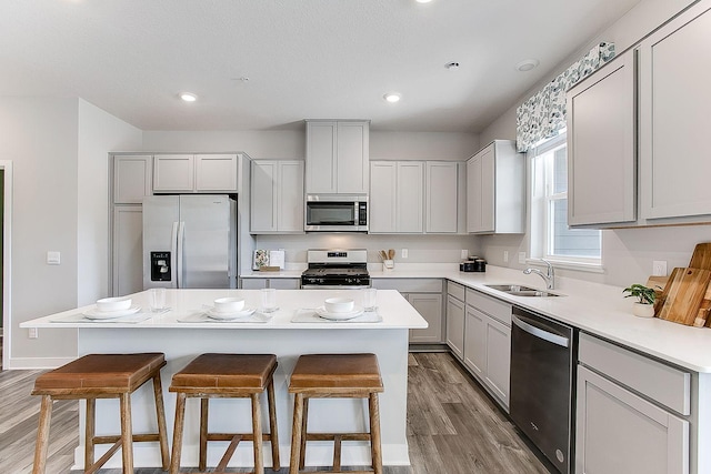 kitchen with a kitchen island, a kitchen bar, light wood-type flooring, a sink, and stainless steel appliances