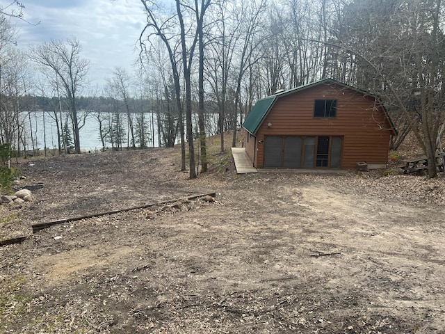 view of yard with a garage, a water view, an outbuilding, and dirt driveway