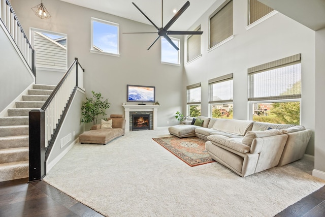 living area featuring visible vents, baseboards, dark wood finished floors, stairs, and a warm lit fireplace