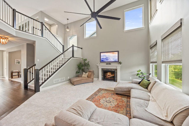 living room featuring visible vents, a warm lit fireplace, wood finished floors, stairway, and baseboards