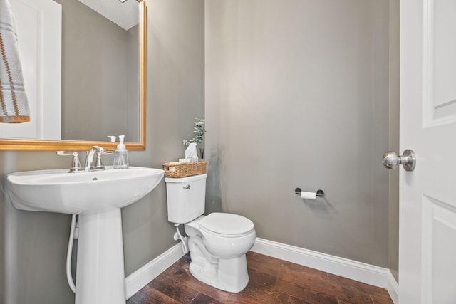 half bath featuring a sink, toilet, baseboards, and wood finished floors