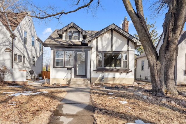 english style home featuring stucco siding, entry steps, and a chimney