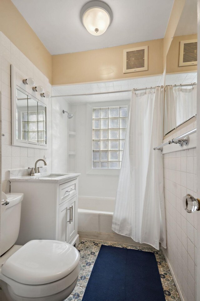 bathroom with visible vents, tile walls, toilet, shower / bath combo with shower curtain, and vanity