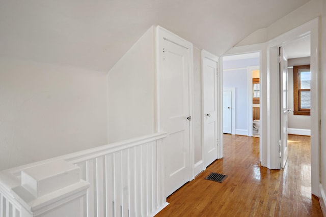 hallway with visible vents, baseboards, vaulted ceiling, and hardwood / wood-style flooring