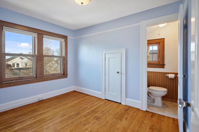 interior space featuring a wainscoted wall, toilet, wood finished floors, and baseboards