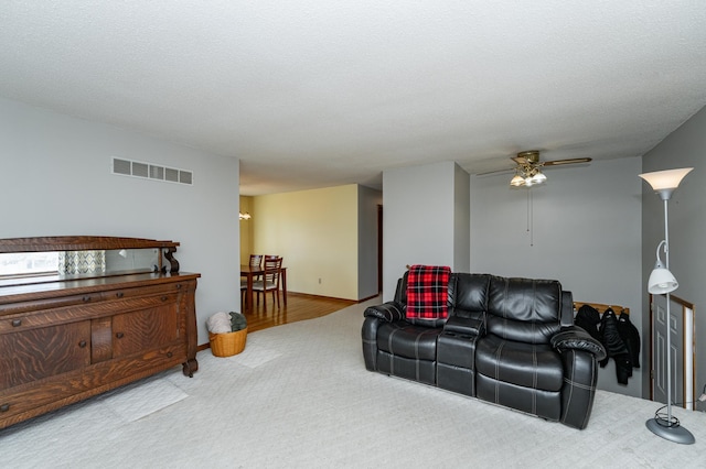 living area featuring visible vents, a textured ceiling, carpet, baseboards, and ceiling fan