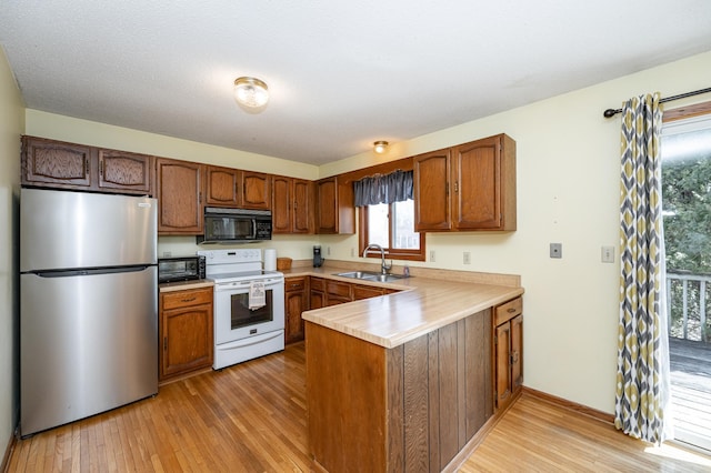 kitchen with black microwave, a peninsula, freestanding refrigerator, electric stove, and a sink