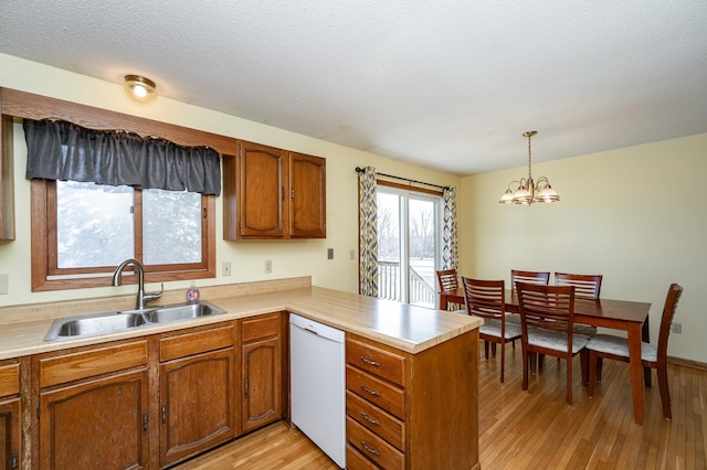 kitchen featuring a peninsula, brown cabinets, white dishwasher, and a sink