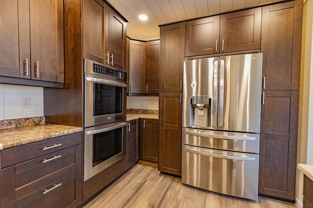 kitchen featuring light wood finished floors, dark brown cabinets, light stone countertops, recessed lighting, and appliances with stainless steel finishes