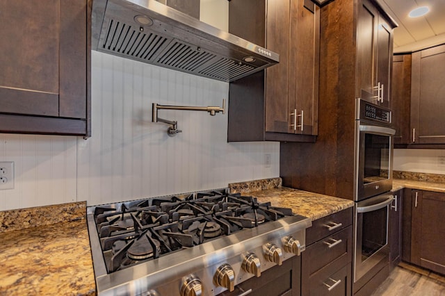 kitchen with light stone counters, dark brown cabinets, range hood, and stainless steel gas cooktop