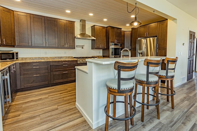 kitchen featuring recessed lighting, appliances with stainless steel finishes, wall chimney exhaust hood, light wood finished floors, and light countertops