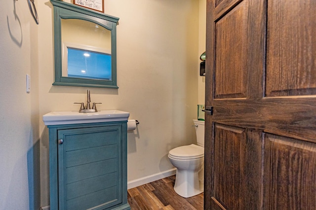 half bathroom featuring baseboards, toilet, wood finished floors, and vanity