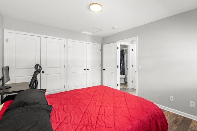 bedroom featuring dark wood-style floors, baseboards, ensuite bath, attic access, and multiple closets