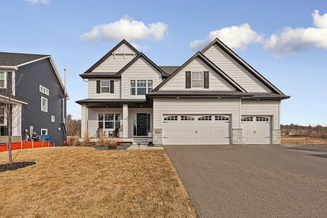 craftsman inspired home featuring aphalt driveway, stone siding, a porch, and a front yard