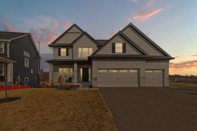 craftsman inspired home with a porch, a lawn, stone siding, and driveway