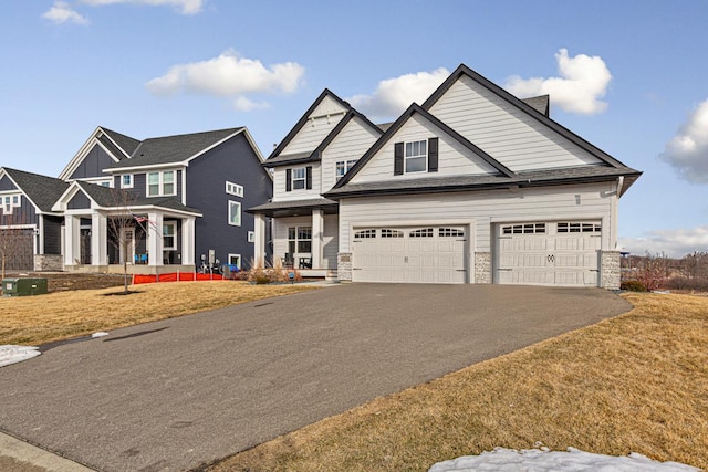 craftsman-style home featuring aphalt driveway, a garage, stone siding, and a front yard