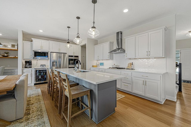 kitchen featuring light wood-type flooring, a kitchen breakfast bar, stainless steel appliances, wine cooler, and wall chimney range hood