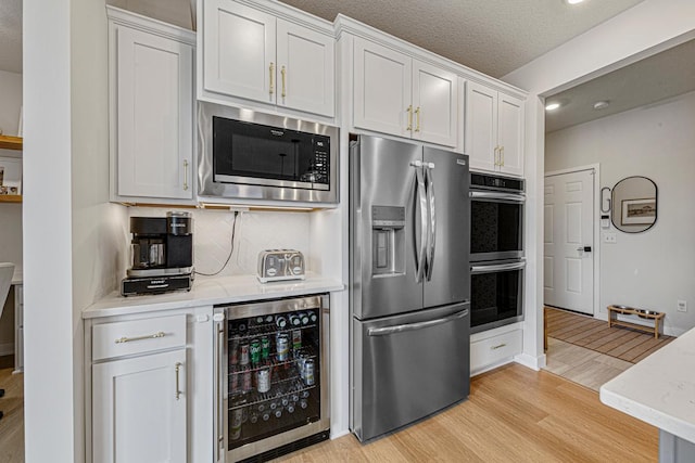 kitchen featuring stainless steel appliances, wine cooler, white cabinets, light wood finished floors, and decorative backsplash