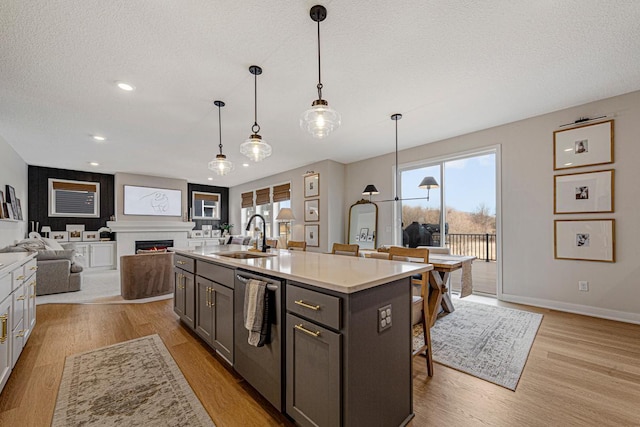 kitchen with light wood finished floors, dishwasher, a lit fireplace, a textured ceiling, and a sink