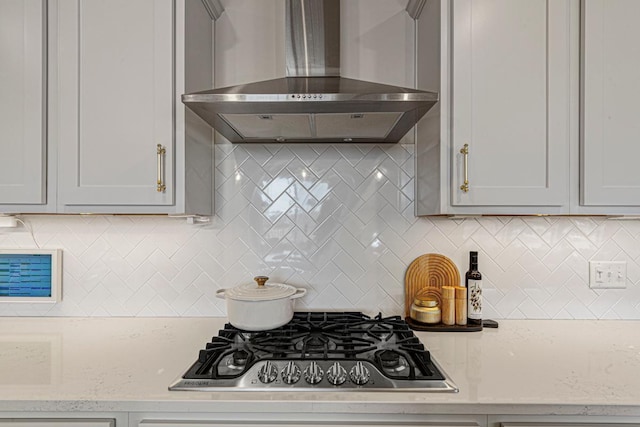 kitchen with decorative backsplash, wall chimney range hood, light stone counters, and stainless steel gas cooktop