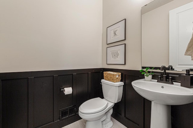 bathroom with visible vents, wainscoting, toilet, and a decorative wall