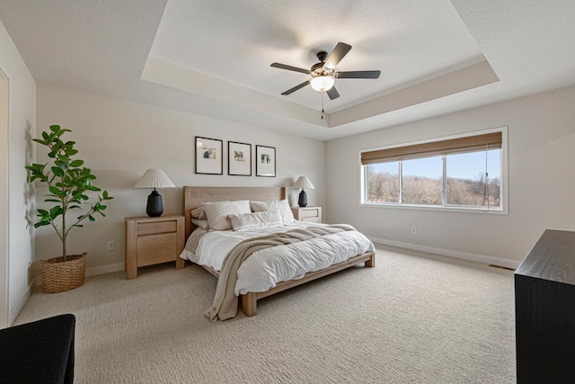 bedroom with light carpet, a textured ceiling, a raised ceiling, and baseboards