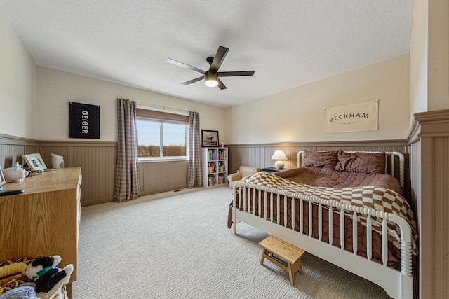 bedroom with a ceiling fan, carpet floors, a textured ceiling, and wainscoting