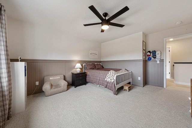 carpeted bedroom featuring a textured ceiling, a wainscoted wall, and ceiling fan