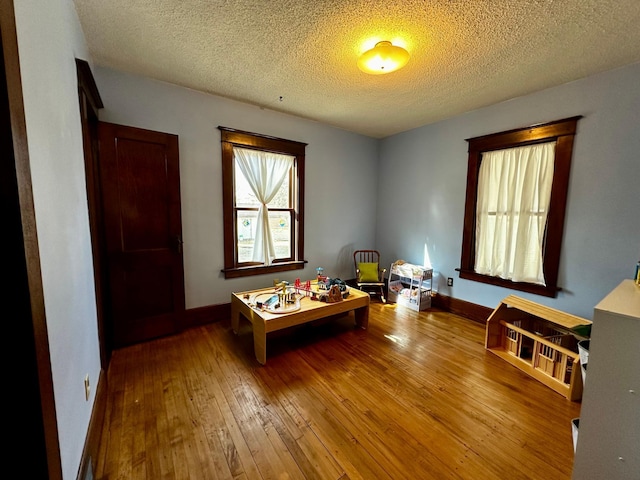 rec room featuring baseboards, a textured ceiling, and hardwood / wood-style flooring