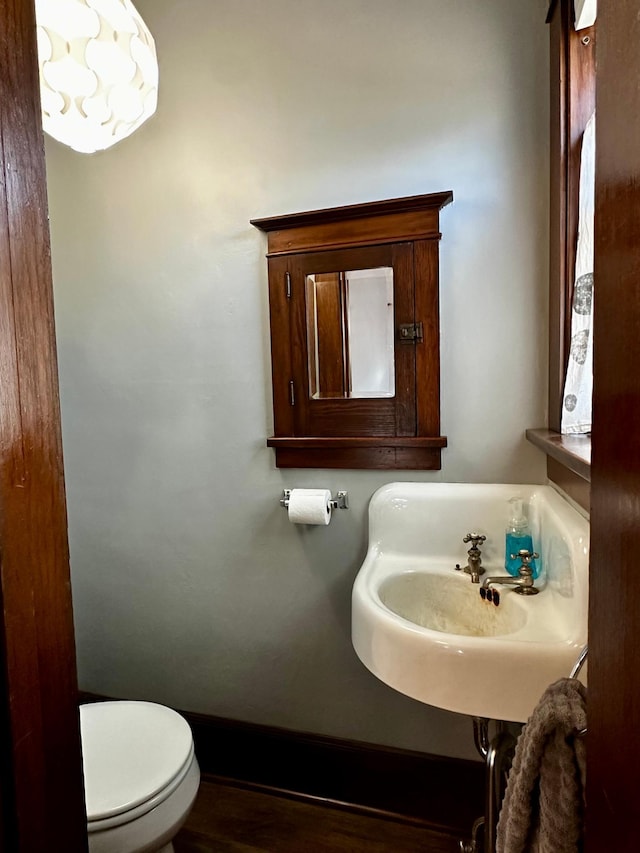 half bathroom featuring toilet, baseboards, and a sink