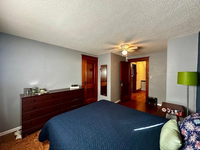 bedroom with a textured ceiling, a ceiling fan, baseboards, and wood finished floors