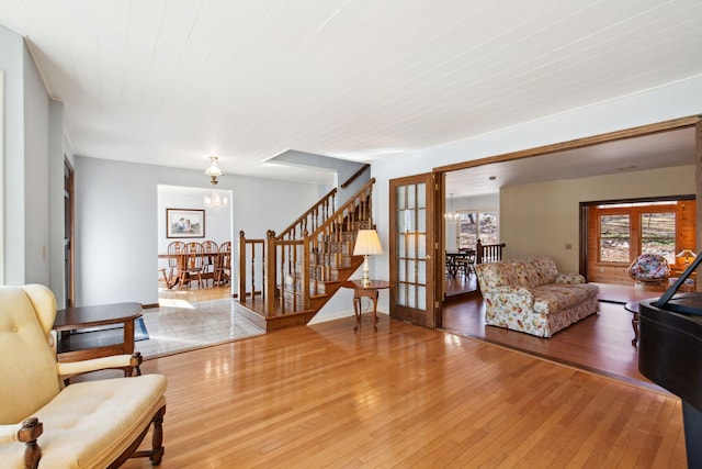 living room with a chandelier, stairway, light wood-style flooring, and french doors