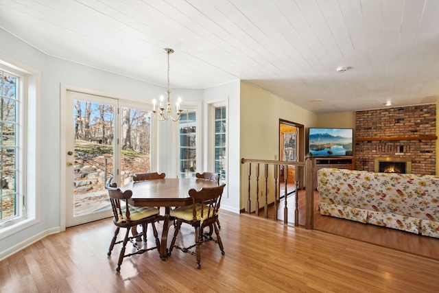 dining room with a chandelier, a healthy amount of sunlight, a brick fireplace, and wood finished floors