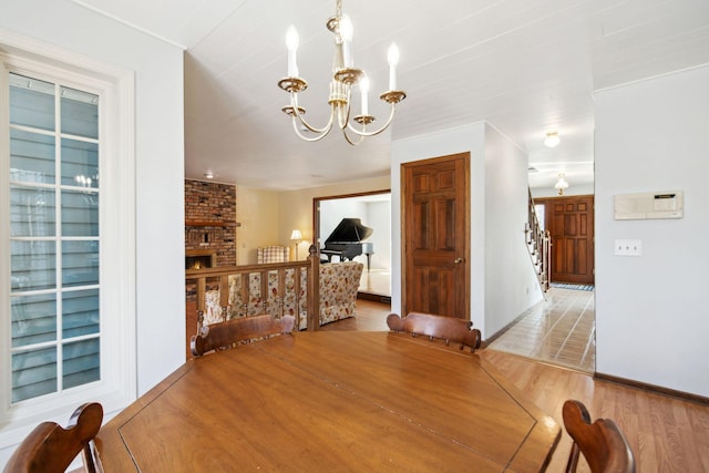 dining room with a brick fireplace, stairs, light wood-type flooring, and an inviting chandelier