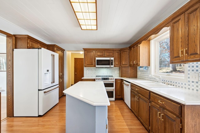 kitchen with white appliances, light wood finished floors, a sink, light countertops, and a center island