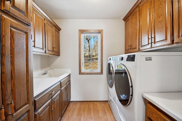 laundry area featuring wallpapered walls, washing machine and dryer, cabinet space, a textured ceiling, and a sink