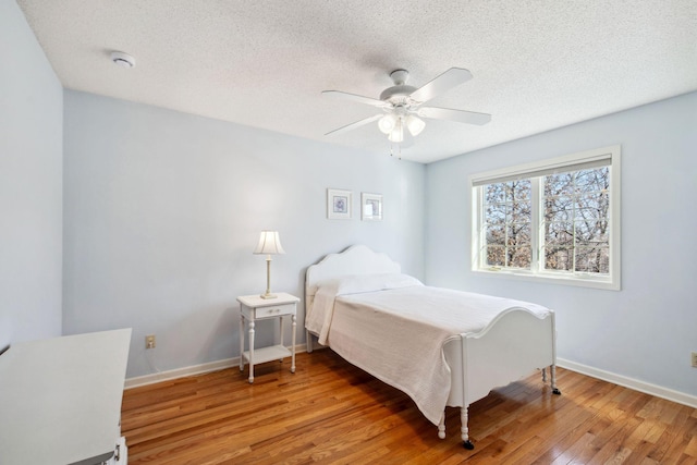 bedroom featuring light wood finished floors, ceiling fan, a textured ceiling, and baseboards