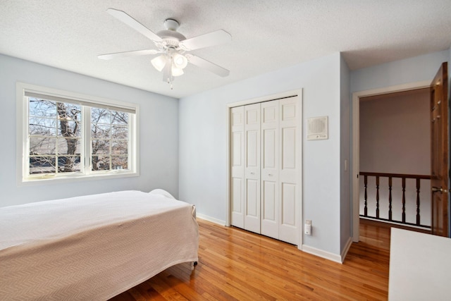 bedroom with light wood-style flooring, a ceiling fan, a textured ceiling, a closet, and baseboards