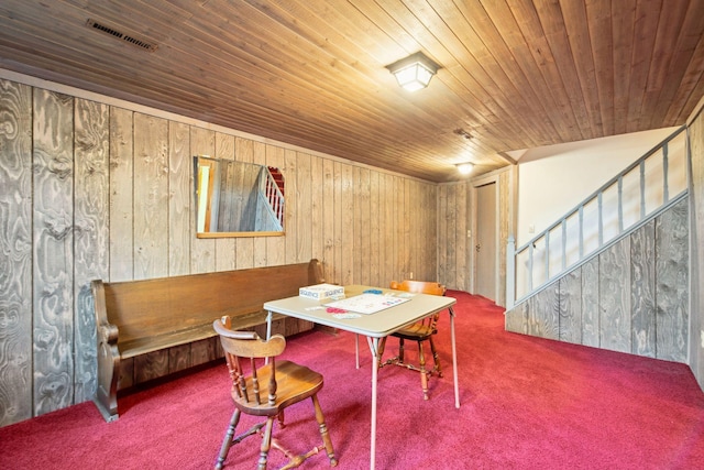 carpeted dining space with visible vents, wood walls, wooden ceiling, and stairs