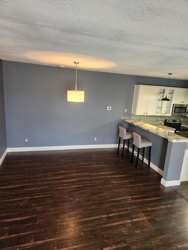 kitchen with a breakfast bar, a peninsula, dark wood finished floors, stainless steel appliances, and glass insert cabinets