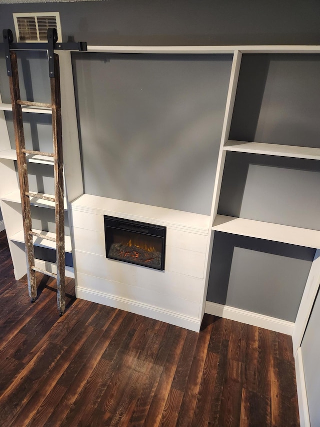 unfurnished living room with a glass covered fireplace, visible vents, a barn door, and wood finished floors