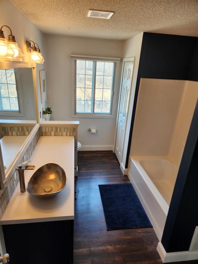 bathroom with toilet, a tub to relax in, a textured ceiling, wood finished floors, and vanity