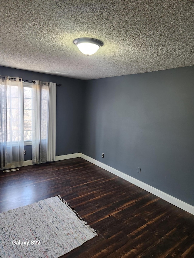 spare room with visible vents, baseboards, a textured ceiling, and dark wood-style flooring