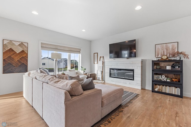 living area with recessed lighting, a glass covered fireplace, and light wood-style flooring