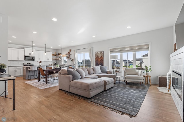 living room featuring recessed lighting, light wood-type flooring, baseboards, and a glass covered fireplace