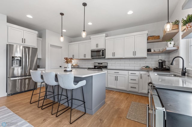 kitchen featuring a breakfast bar, open shelves, a sink, stainless steel appliances, and light wood-style floors