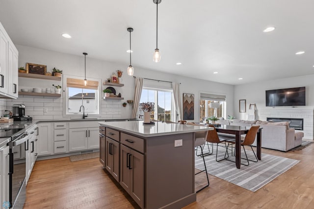 kitchen featuring open shelves, a breakfast bar, light wood-type flooring, electric range oven, and a sink