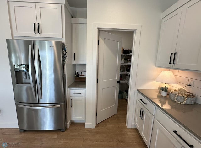 kitchen featuring backsplash, wood finished floors, stainless steel refrigerator with ice dispenser, and white cabinets