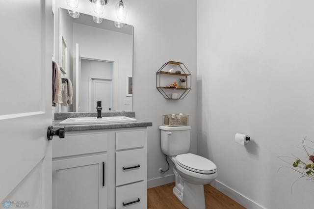 half bathroom with toilet, vanity, baseboards, and wood finished floors