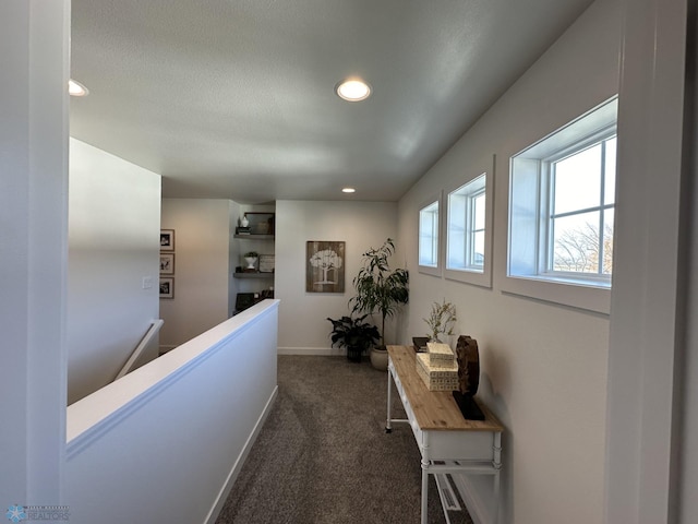 corridor with an upstairs landing, a textured ceiling, recessed lighting, dark colored carpet, and baseboards